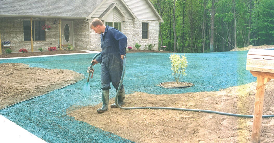 A man in blue overalls spraying water on the ground.